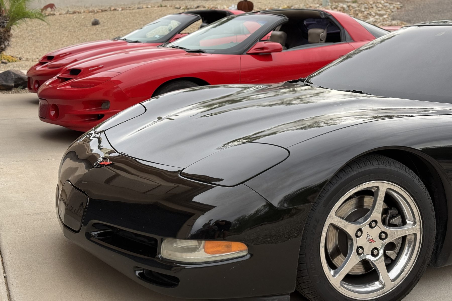 Black C5 Corvette in front of two red fourth-gen Trans Ams, lined up on a driveway